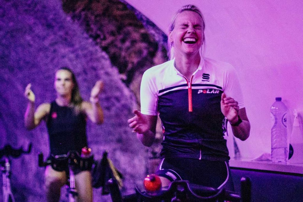 Vrouw moet lachen tijdens les Power Cycle als onderdeel cardio les