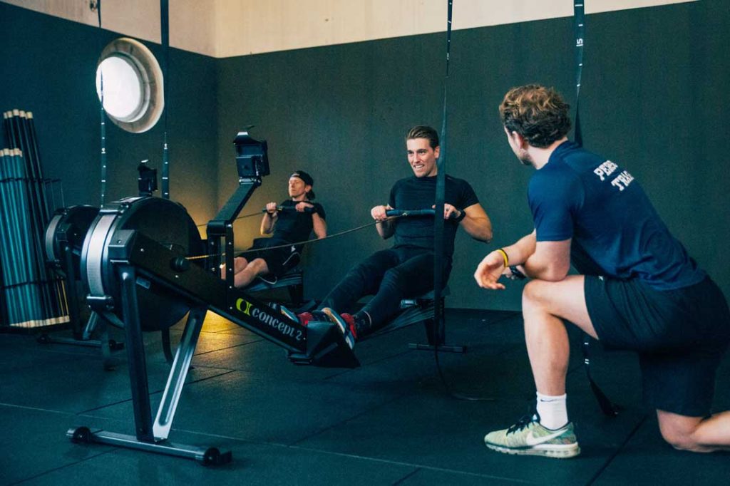 Mensen volgen een fitnessles onder toezicht van een personal trainer bij row en strength
